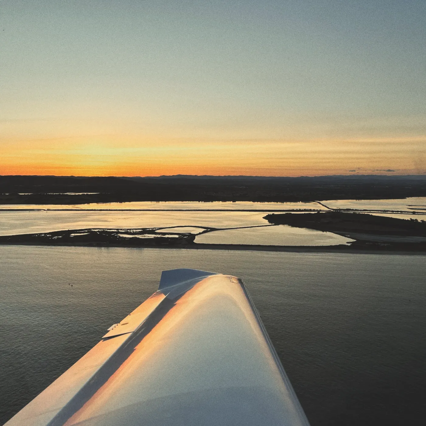 Sunset over a water landscape with a wing in the foreground